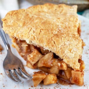 Slice of gluten free apple pie on white plate with fork.