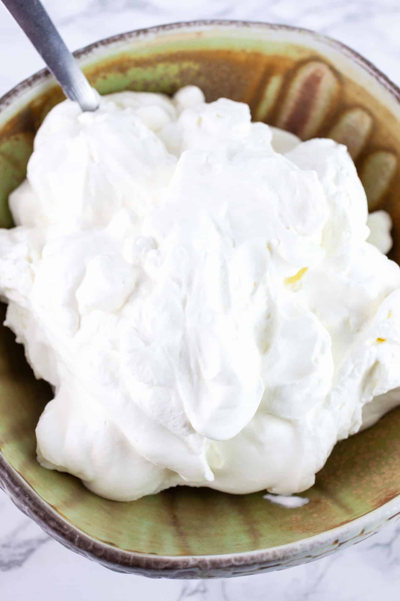 Homemade whipped cream in ceramic bowl with spoon.
