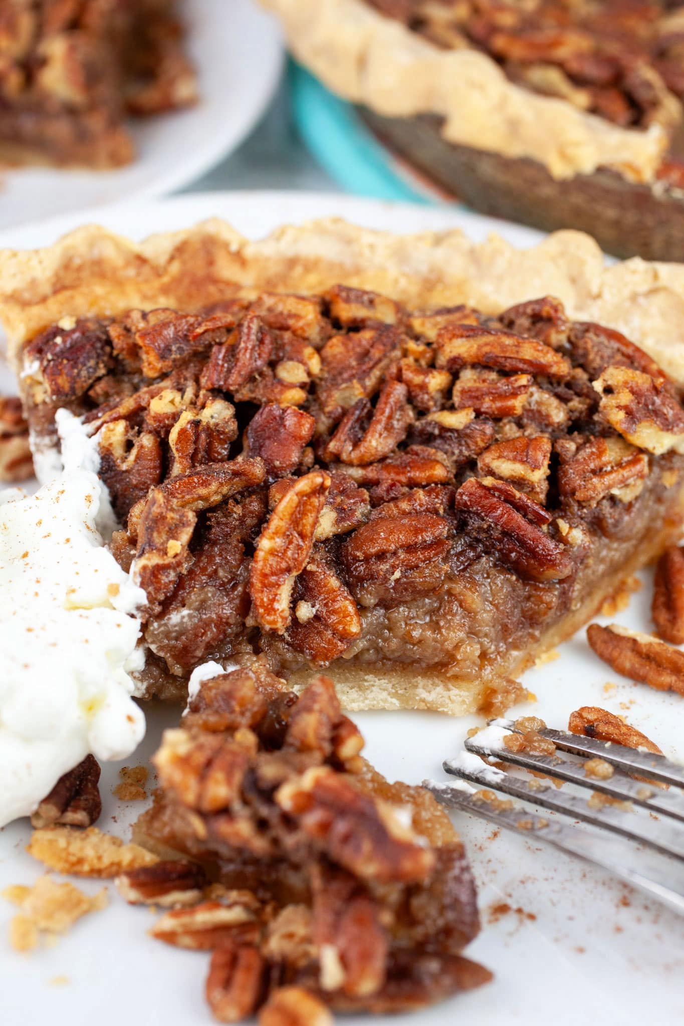 Slice of maple bourbon walnut pie with whipped cream on white plate cut with fork.