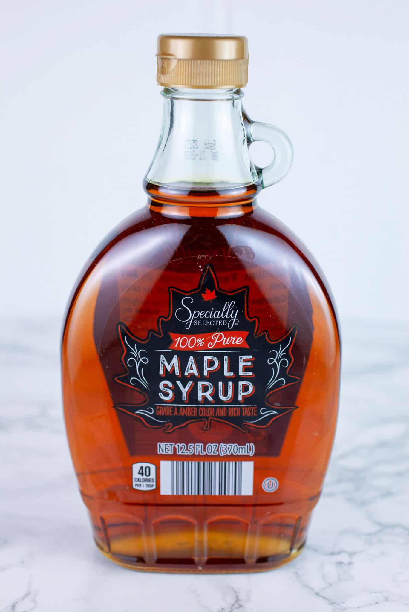 Unopened bottle of maple syrup on white surface.