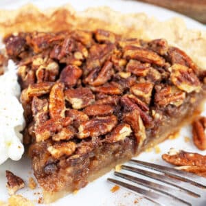 Slice of maple bourbon pecan pie with whipped cream on white plate with fork.