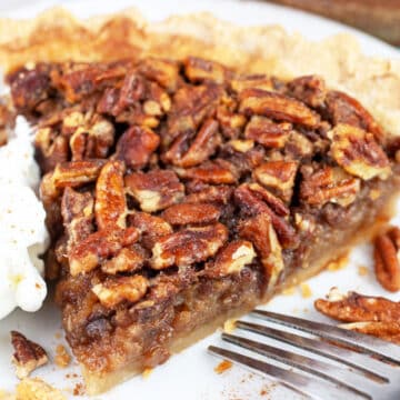 Slice of maple bourbon pecan pie with whipped cream on white plate with fork.