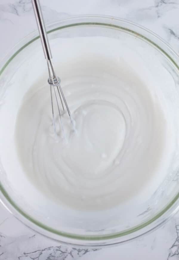 Coconut milk in glass bowl with small whisk.