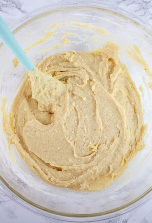 Coconut cupcake batter in glass bowl with spatula.