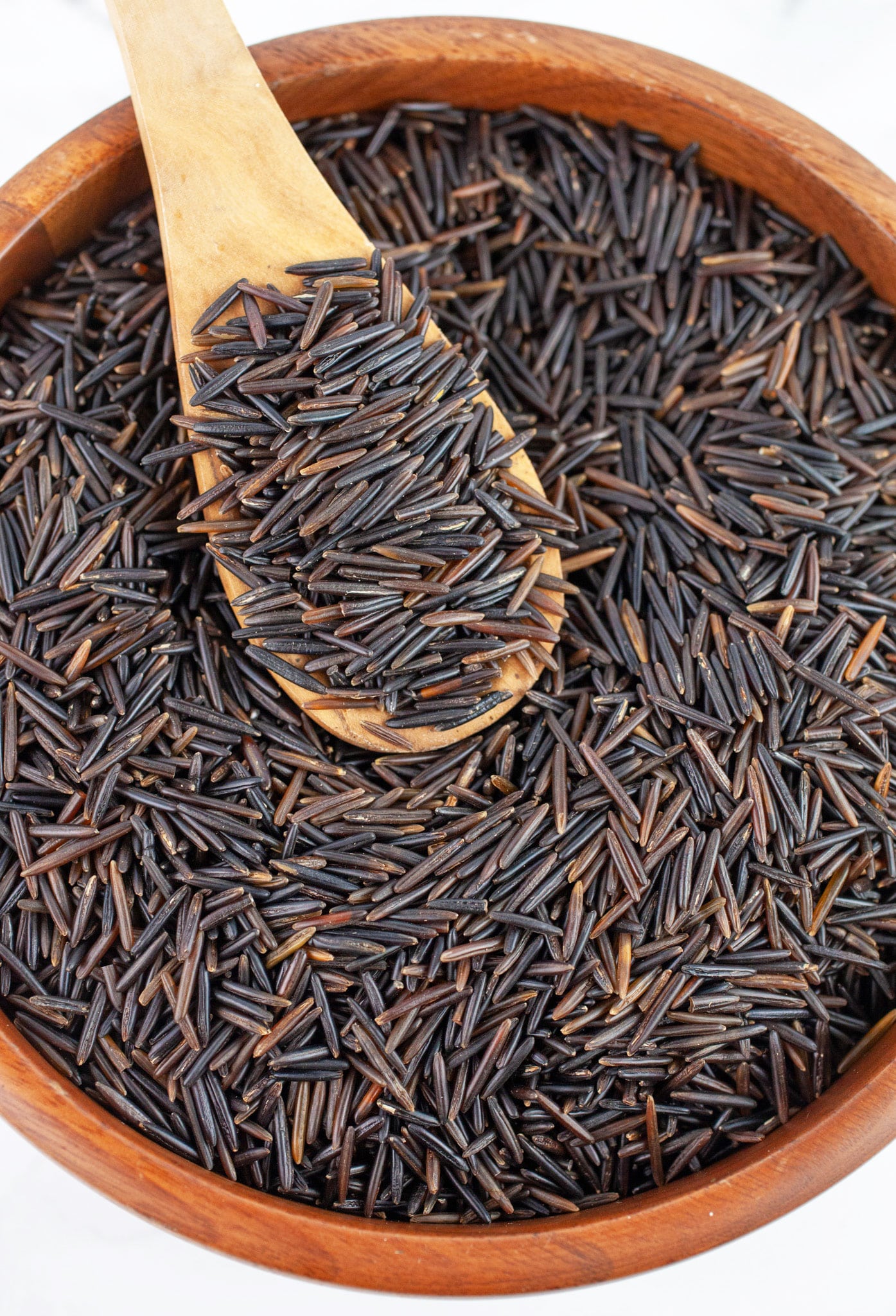Uncooked wild rice in wooden bowl with wooden spoon.