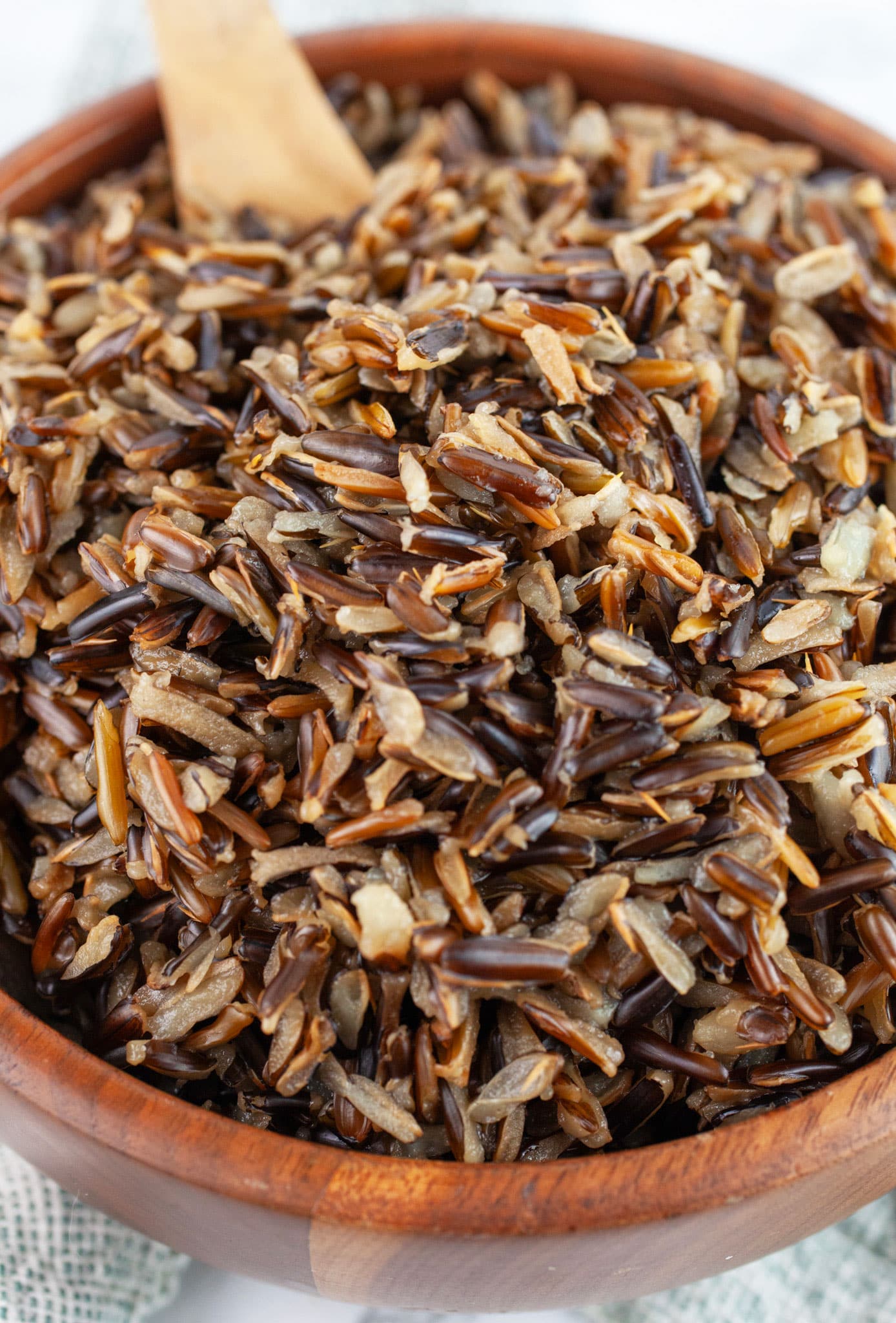 Cooked wild rice in wooden bowl with wooden spoon.