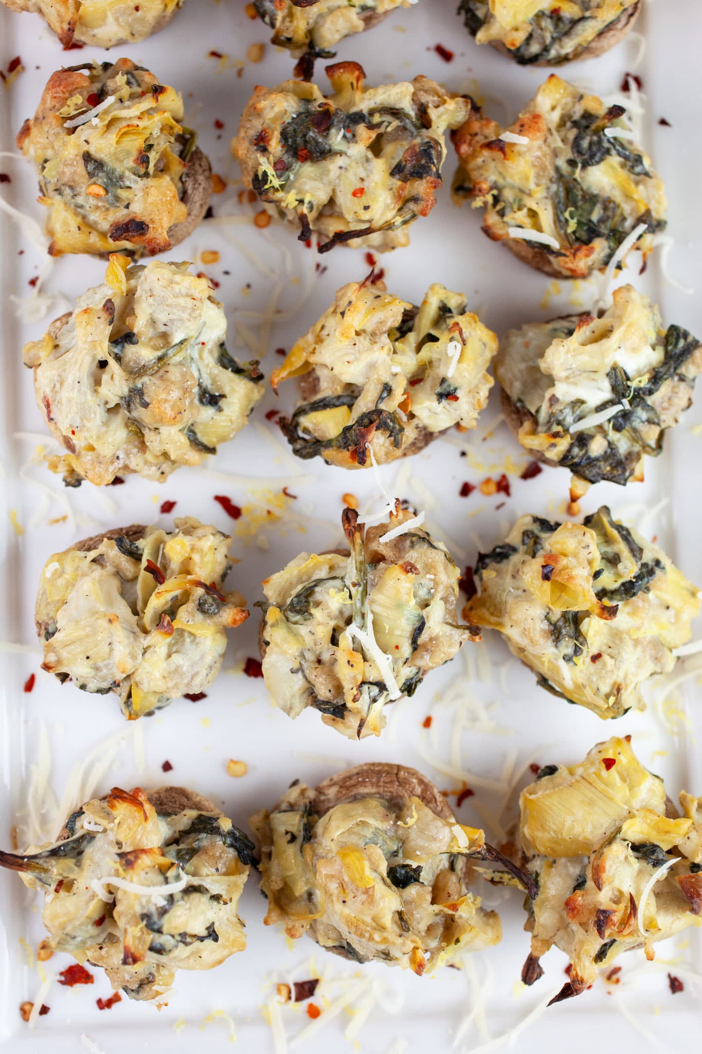 Spinach artichoke stuffed mushrooms on white serving platter.