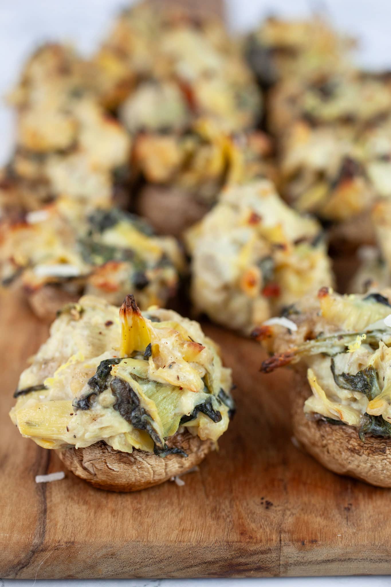 Spinach artichoke stuffed mushrooms on wooden serving board.