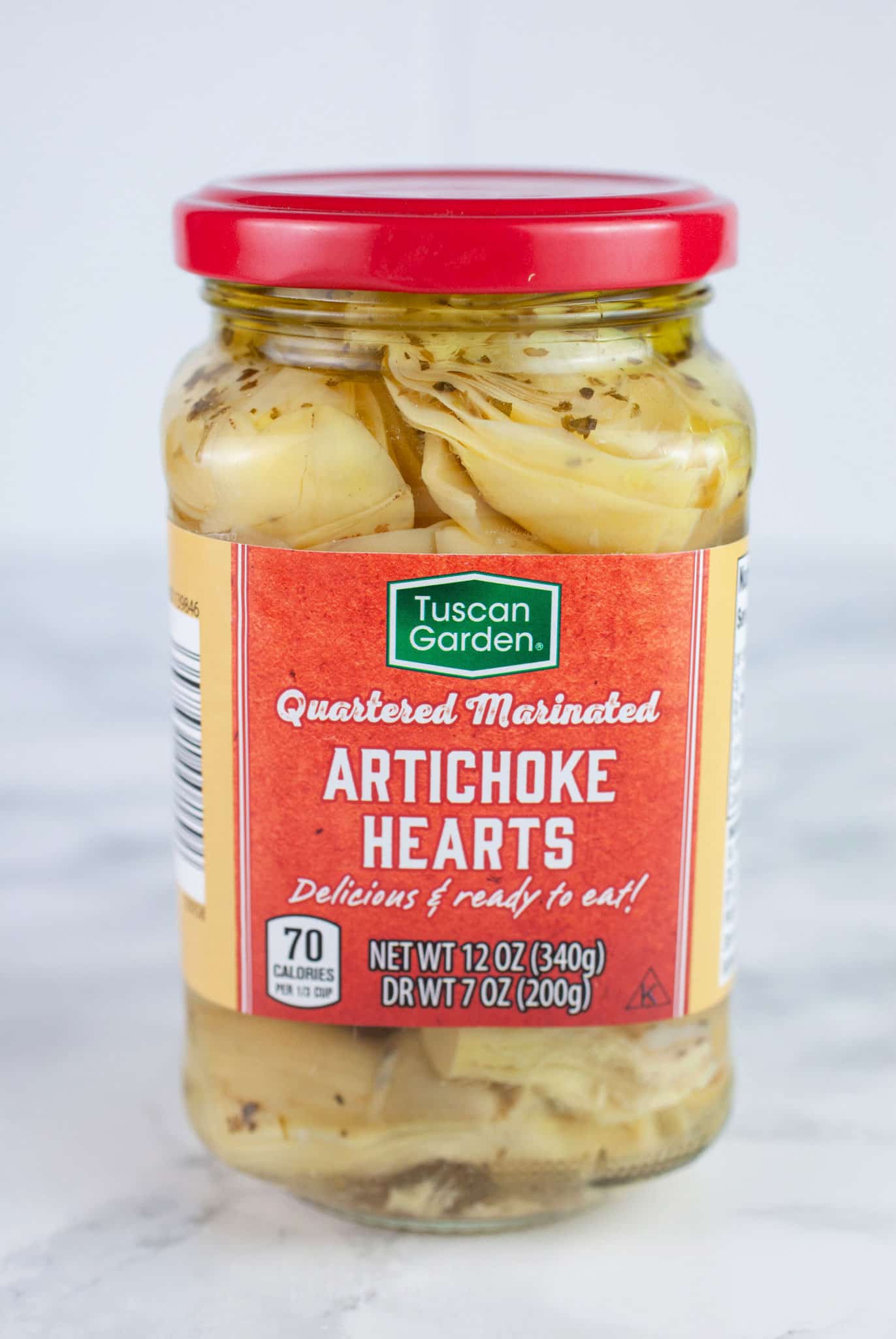 Unopened jar of marinated artichoke hearts on white surface.