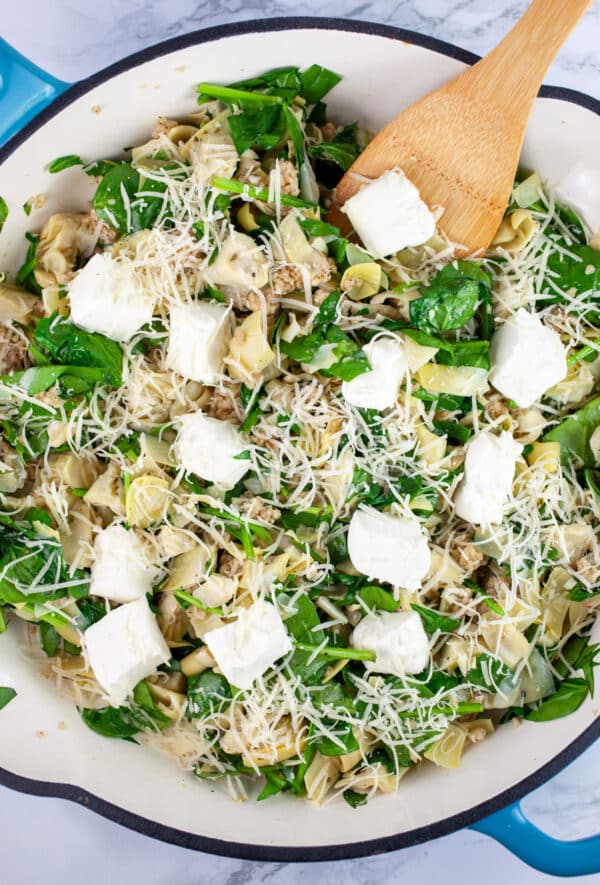 Chopped marinated artichoke hearts, spinach, Parmesan cheese, and cream cheese in skillet with wooden spatula.
