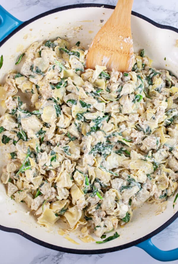 Creamy spinach artichoke filling in skillet with wooden spatula.