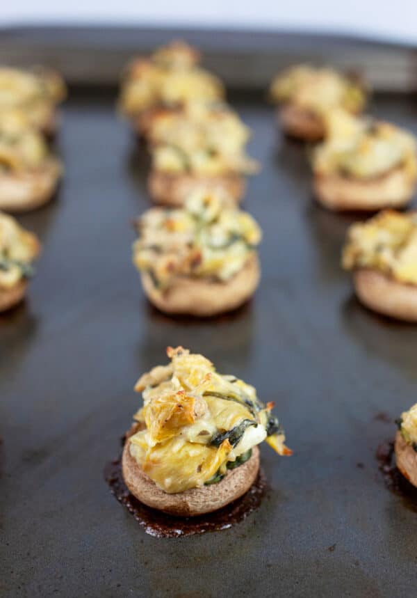 Cooked artichoke spinach stuffed mushrooms on baking sheet.