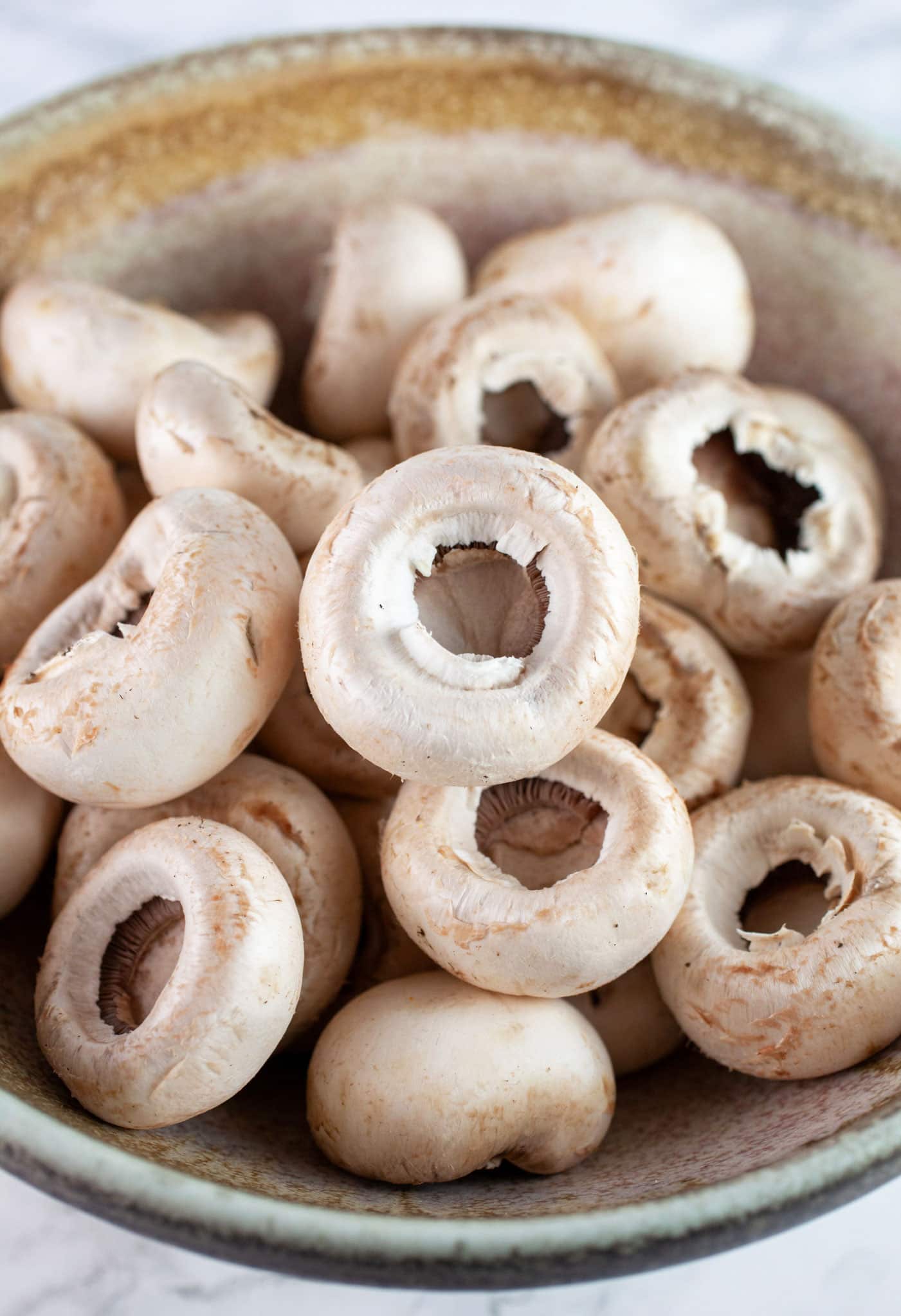 White button mushrooms with stems removed in ceramic bowl.