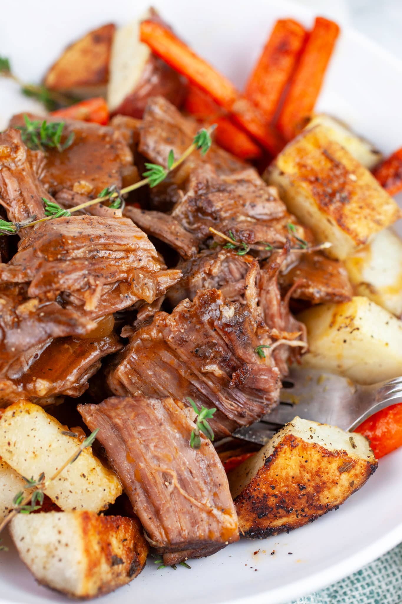 Pot roast with roasted potatoes and carrots in white bowl with fork.