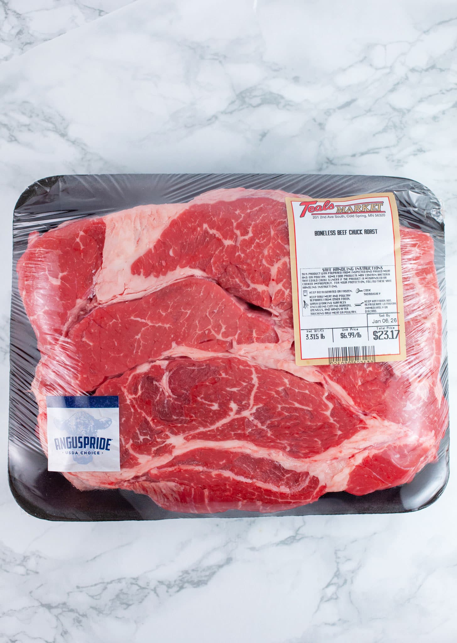 Package of raw beef chuck roast on white surface.