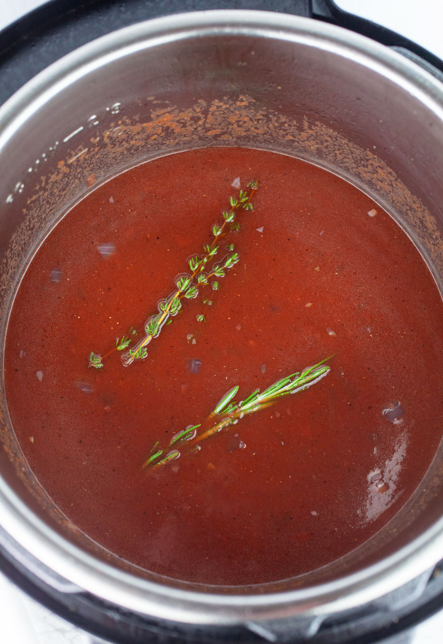 Red wine tomato beef broth mixture with fresh herbs in Instant Pot.