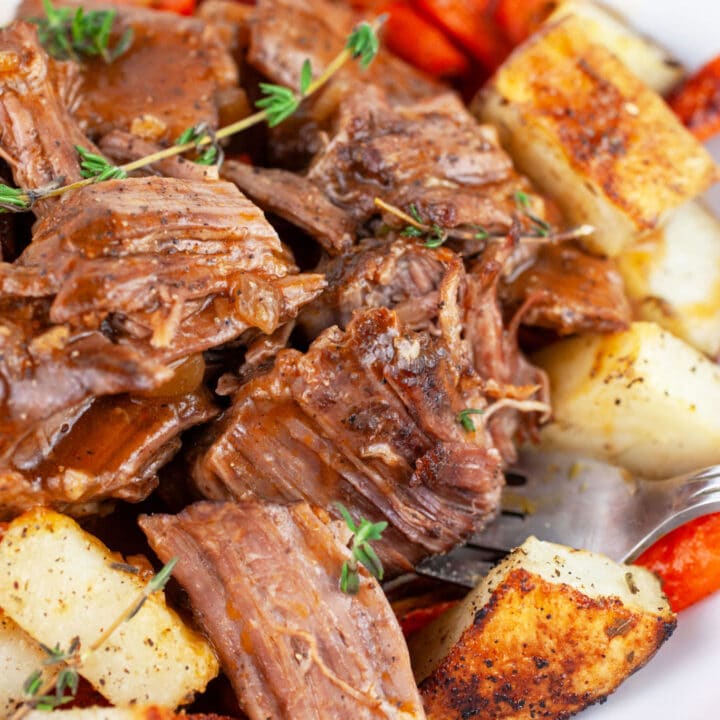 Instant Pot pot roast with gravy and roasted potatoes and carrots in white bowl with fork.