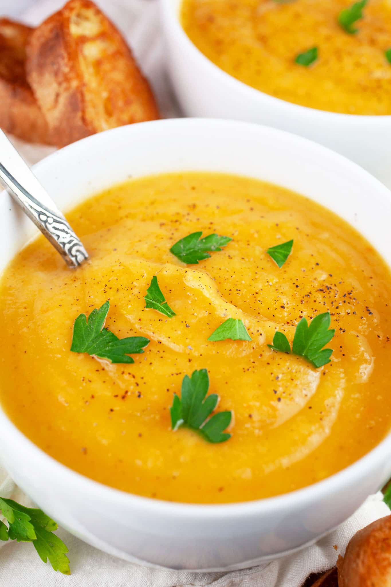 Winter root vegetable soup in white bowl garnished with parsley served with crostini.