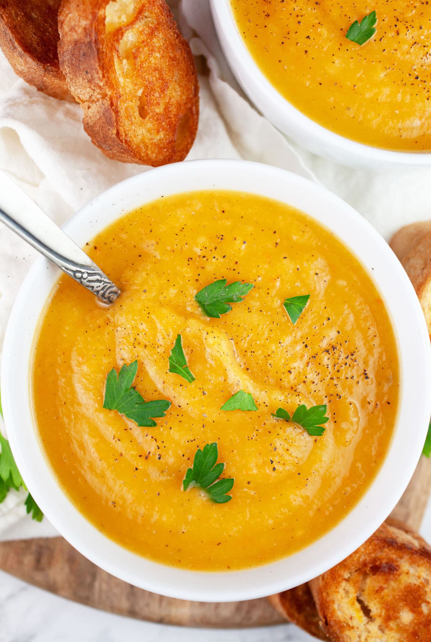 Root vegetable soup in white bowls garnished with parsley served with toasted crostini.