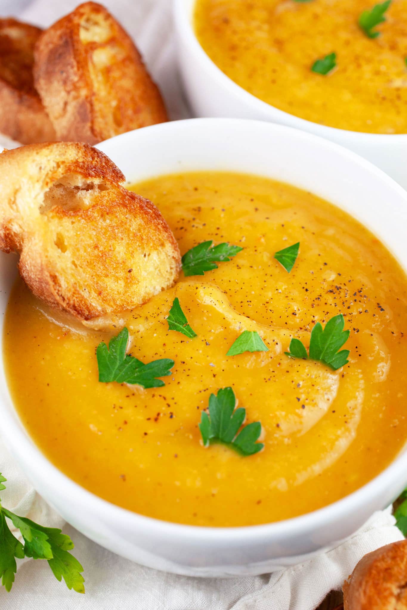 Winter root vegetable soup in white bowls garnished with parsley and served with crostini.