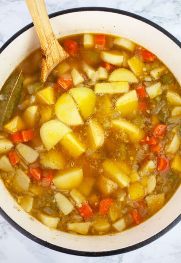 Vegetable soup simmered in Dutch oven with wooden spoon.
