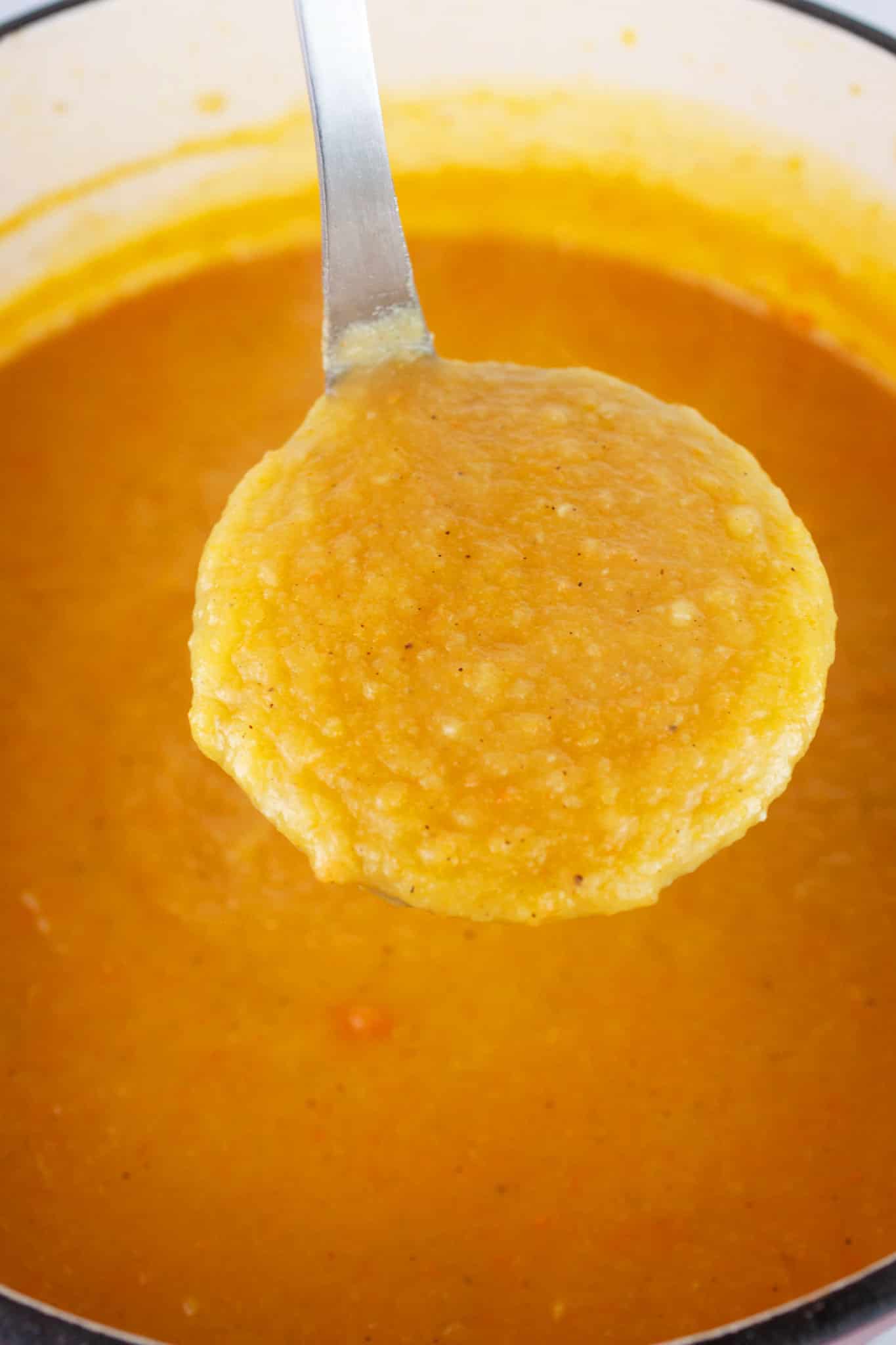 Scoop of pureed root vegetable soup lifted from Dutch oven on metal ladle.