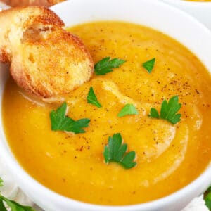 Winter root vegetable soup in white bowl with parsley and crostini.