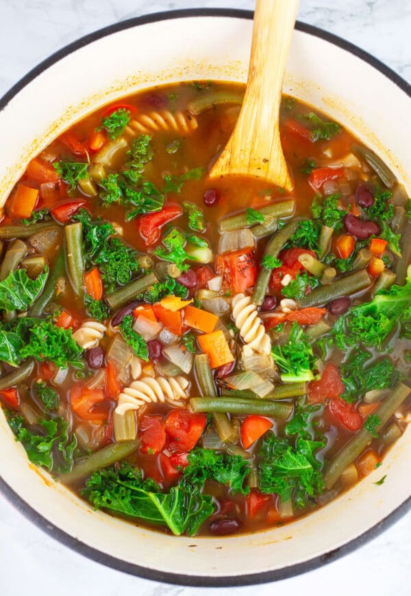 Vegetable noodle soup in Dutch oven with wooden spoon.
