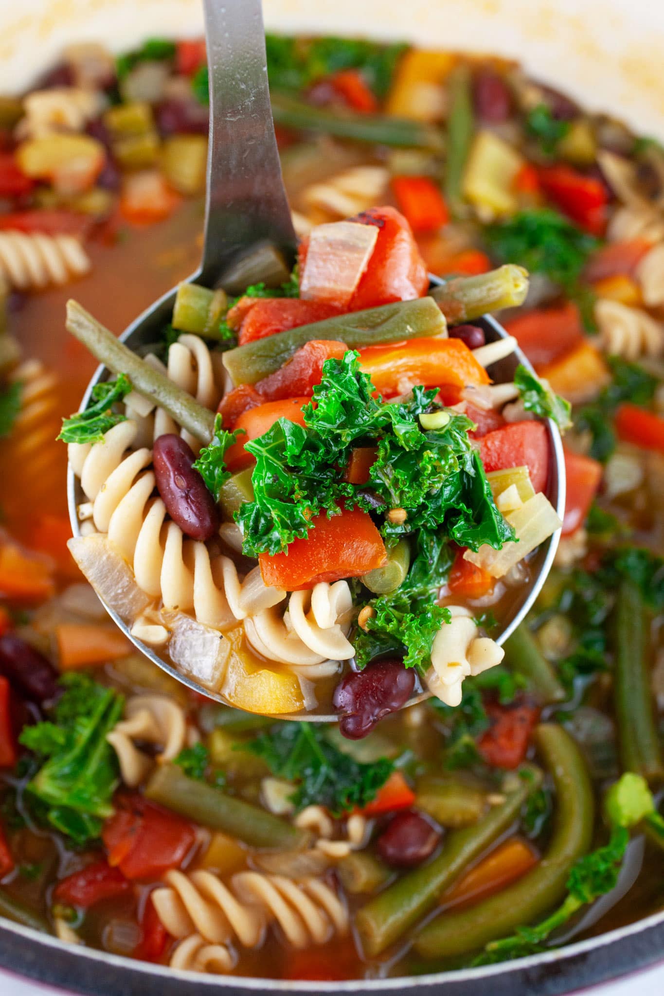 Scoop of Tuscan vegetable soup lifted from Dutch oven on metal ladle.