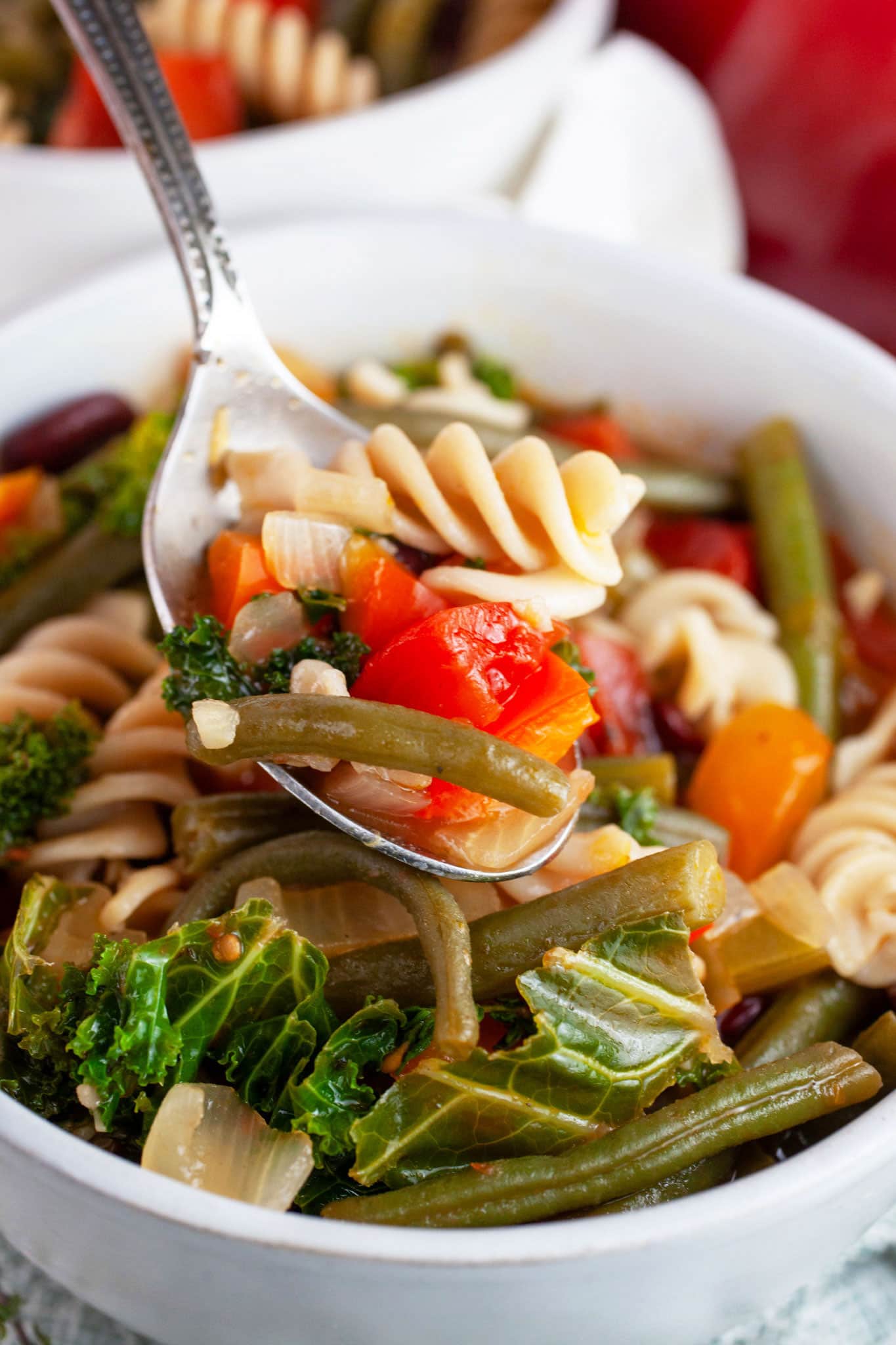 Spoonful of Tuscan veggie soup lifted from white bowl.