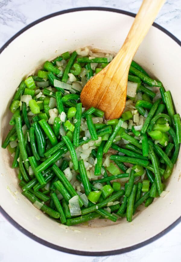 Minced garlic, onions, celery, and chopped green beans sauteed in Dutch oven with wooden spoon.