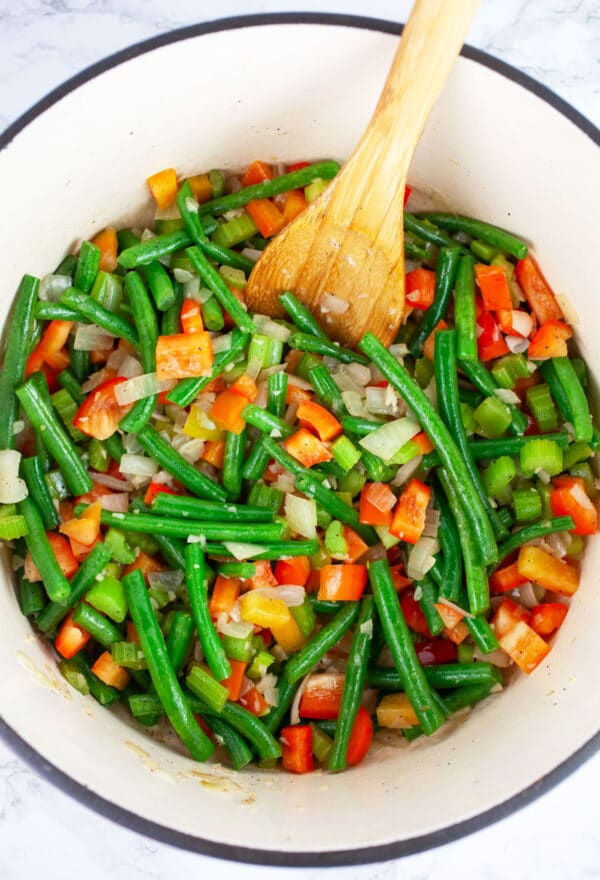 Green beans and diced red bell peppers sauteed in Dutch oven with wooden spoon.