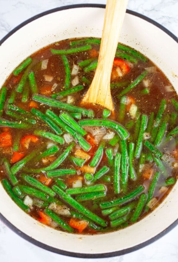 Vegetables and broth in Dutch oven with wooden spoon.