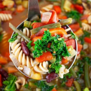 Scoop of Tuscan vegetable soup lifted from Dutch oven with metal ladle.