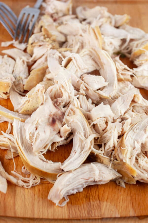 Cooked, shredded chicken breasts on wooden cutting board with two forks.