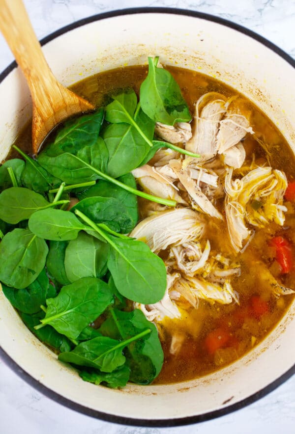 Asian chicken soup with fresh spinach in Dutch oven with wooden spoon.