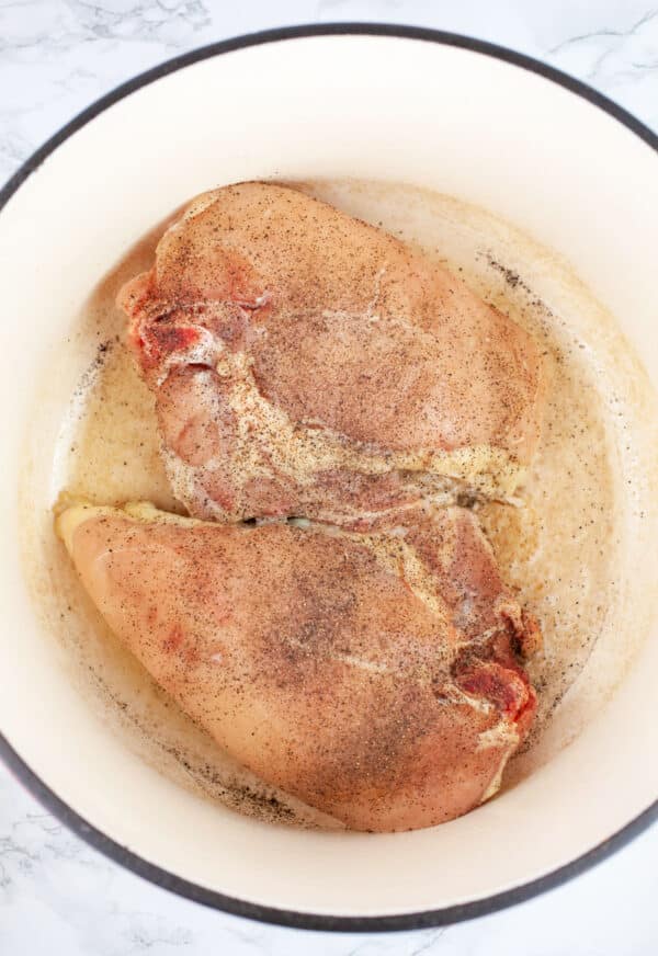 Raw split chicken breasts sauteed in Dutch oven.