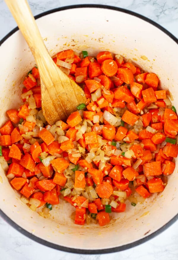 Minced garlic, onions, ginger, and jalapenos and chopped carrots sauteed in Dutch oven with wooden spoon.
