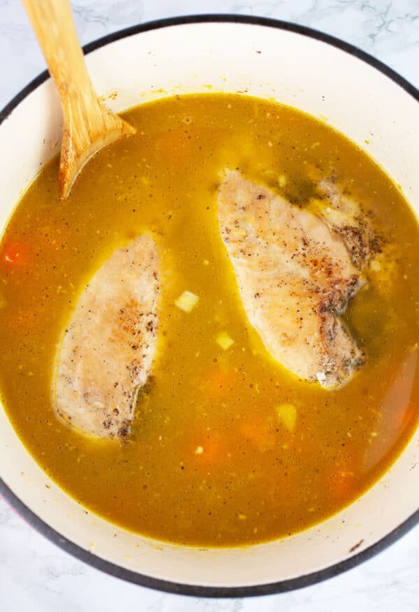 Uncooked chicken soup in Dutch oven with wooden spoon.