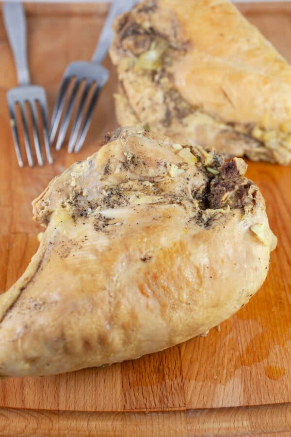 Cooked split chicken breasts on wooden cutting board with two forks.