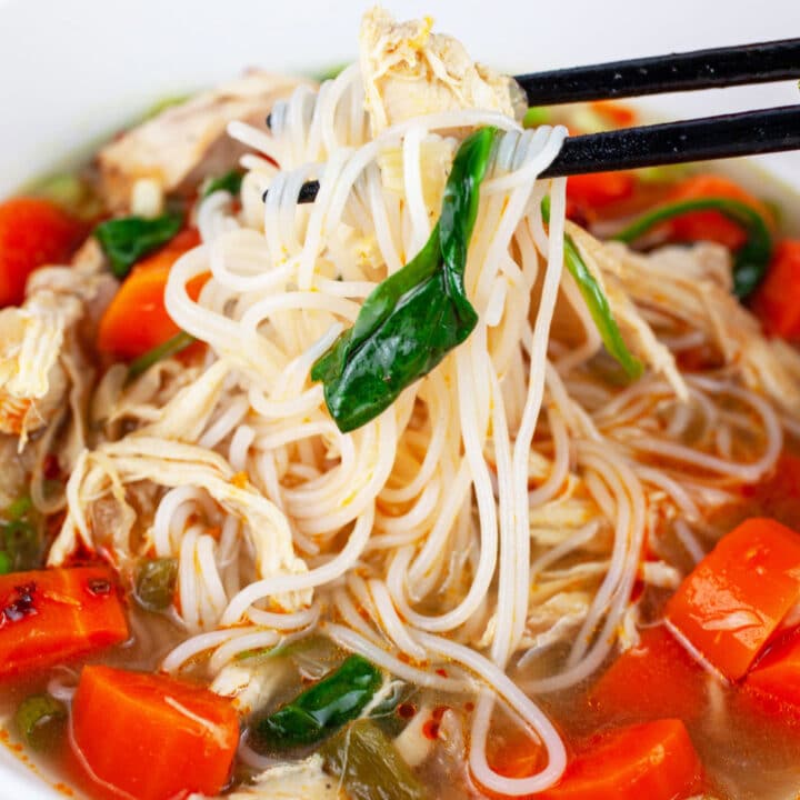 Chopsticks lifting noodles from bowl of Asian chicken soup.