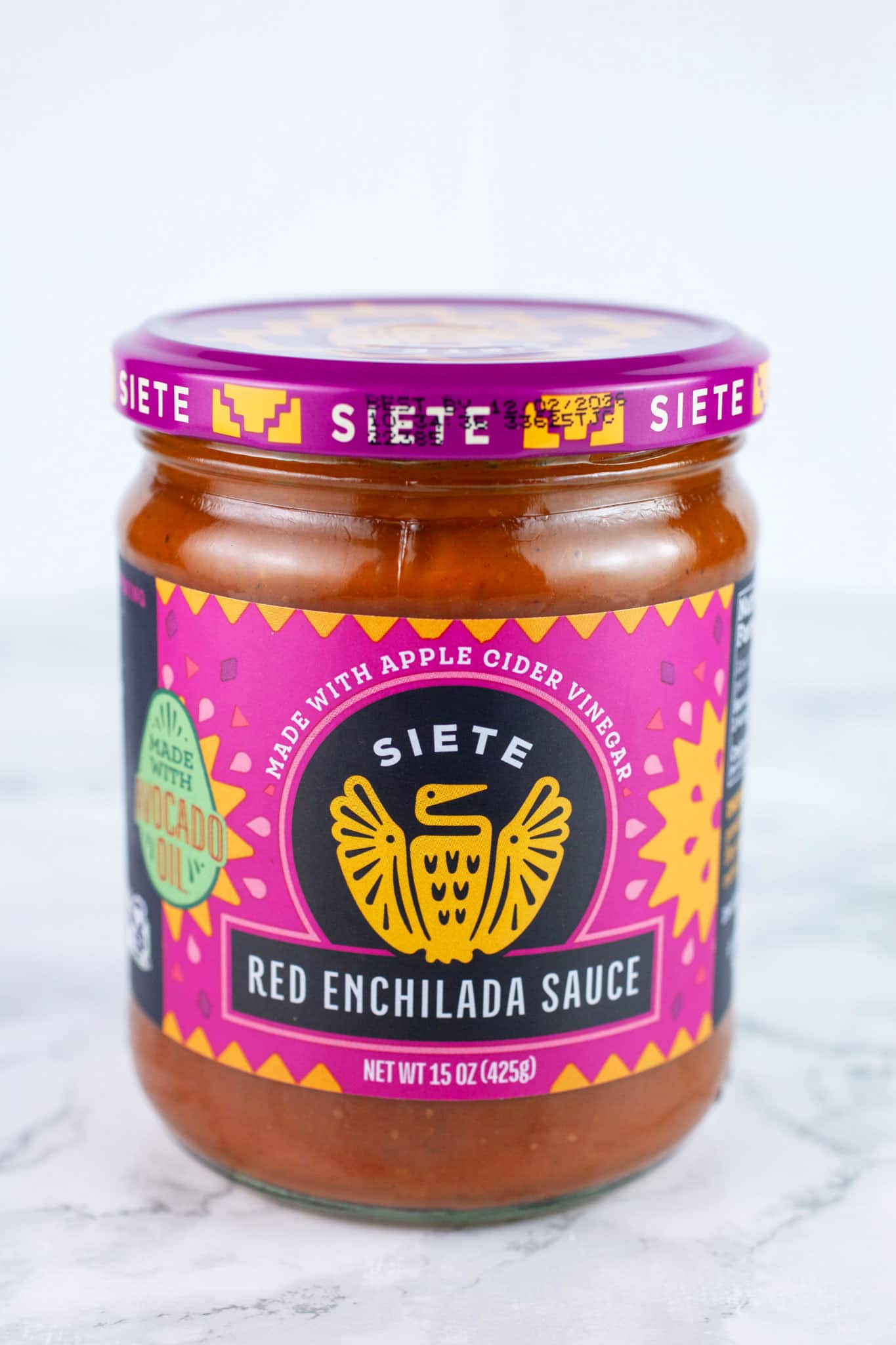 Unopened jar of red enchilada sauce on white surface.