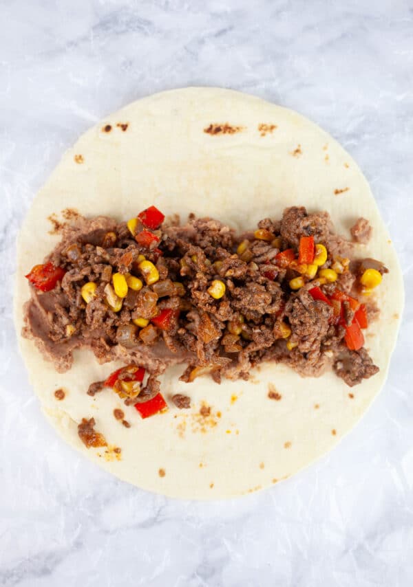 Refried beans and cooked ground beef mixture on tortilla.