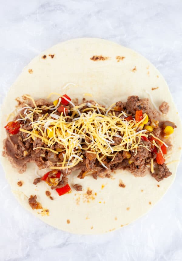 Refried beans, cooked ground beef, and shredded cheese on tortilla.