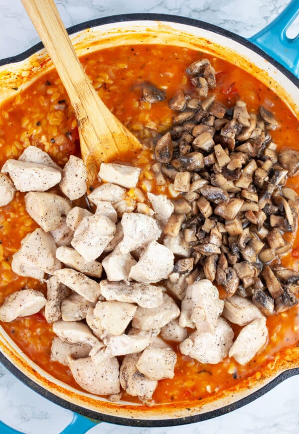 Cooked chicken and mushrooms added to skillet with orzo pasta with wooden spoon.