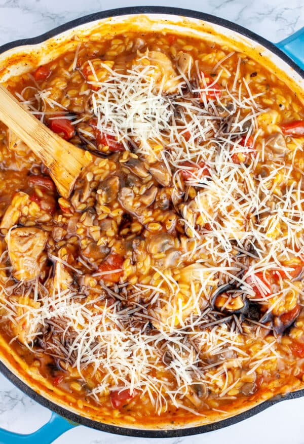 Orzo pasta with grated Parmesan cheese and balsamic vinegar in skillet with wooden spoon.