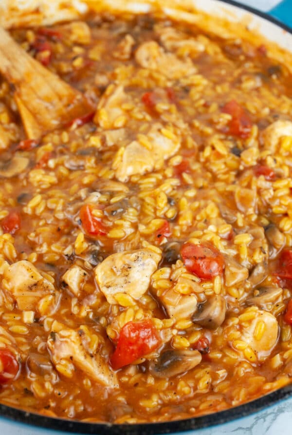 Chicken mushroom and tomato pasta in skillet with wooden spoon.
