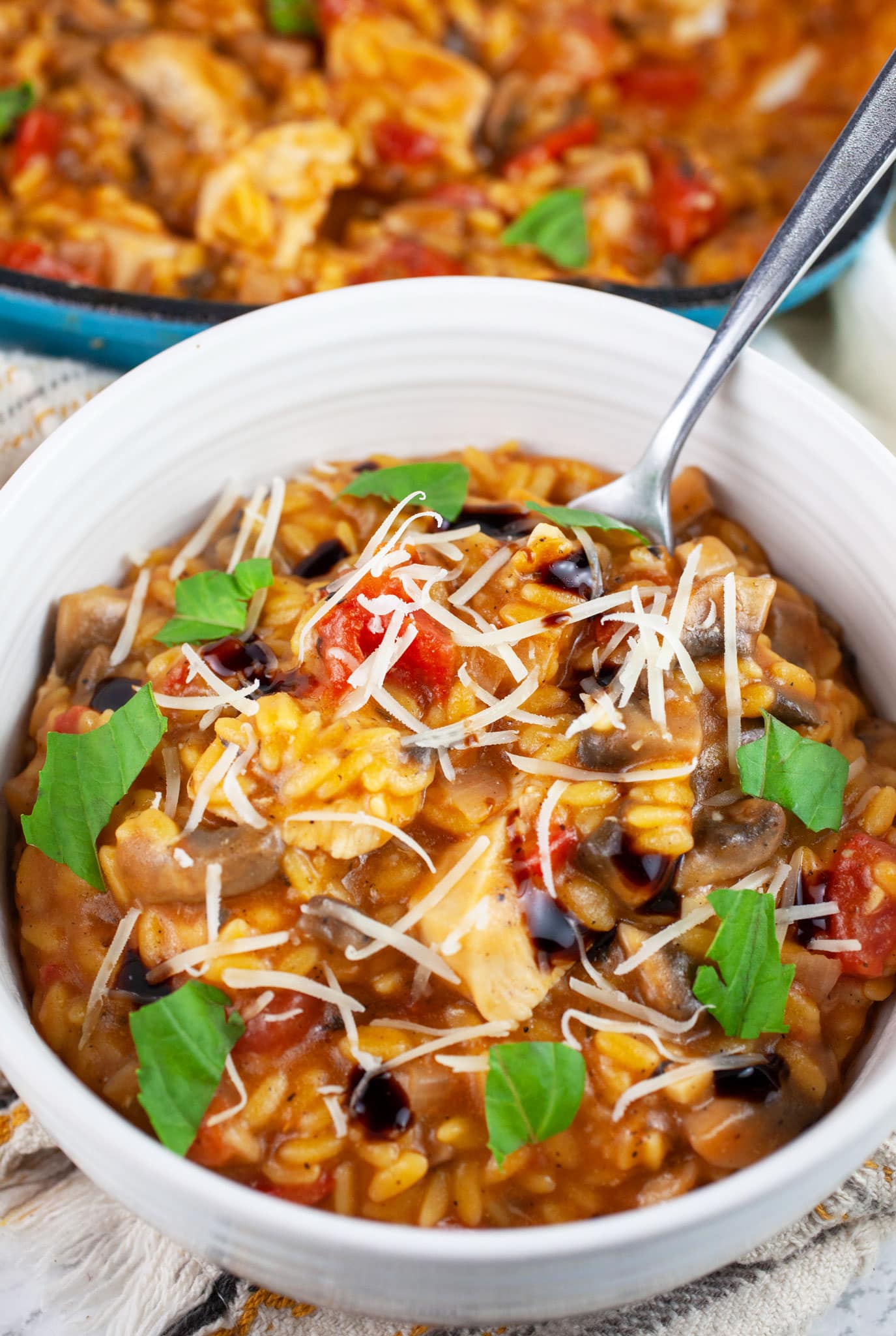 Chicken mushroom tomato pasta in white bowl with fork garnished with Parmesan cheese, fresh basil, and balsamic glaze.