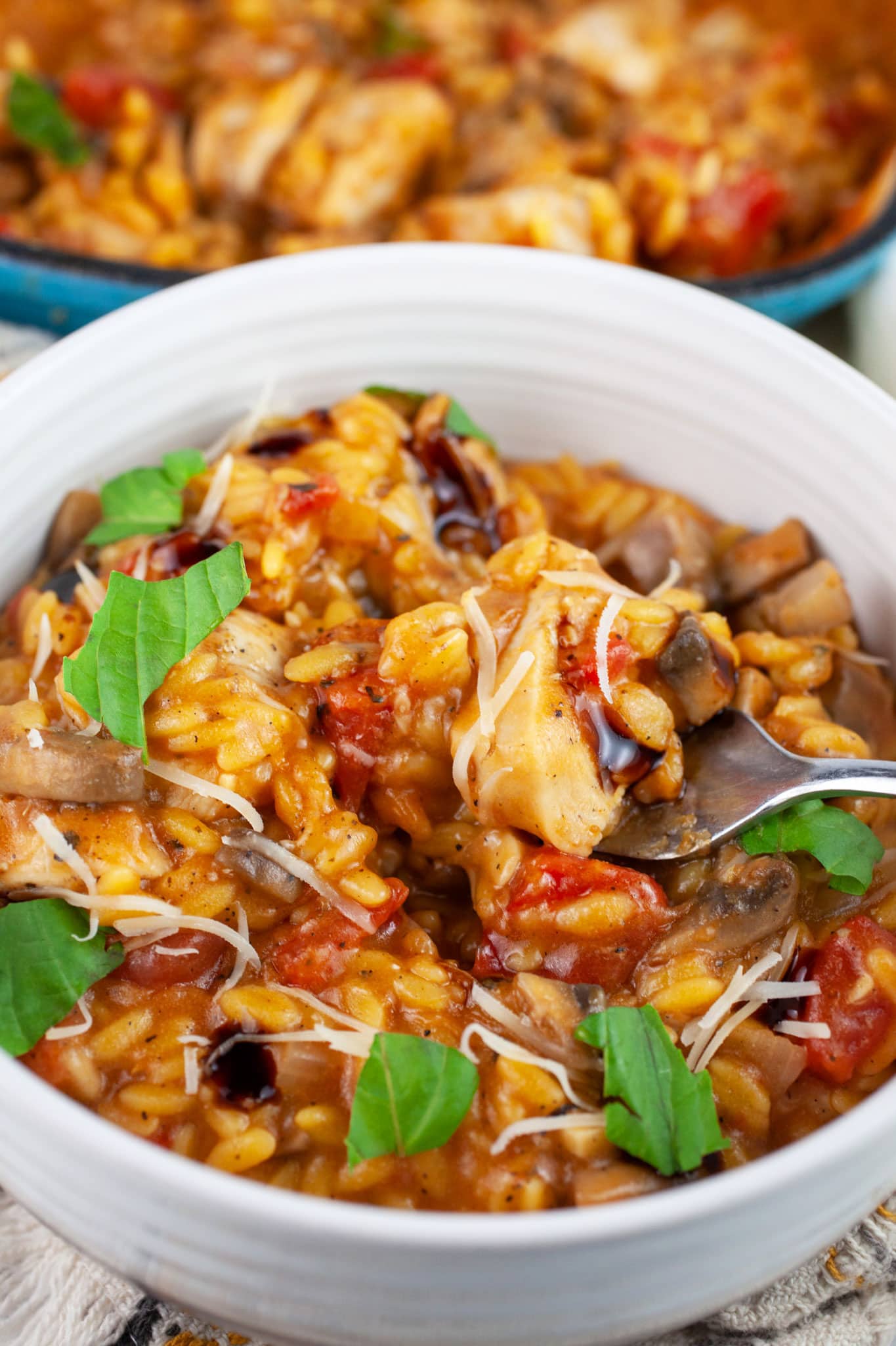 Chicken mushroom tomato pasta garnished with balsamic glaze, Parmesan cheese and fresh basil in white bowl with fork.