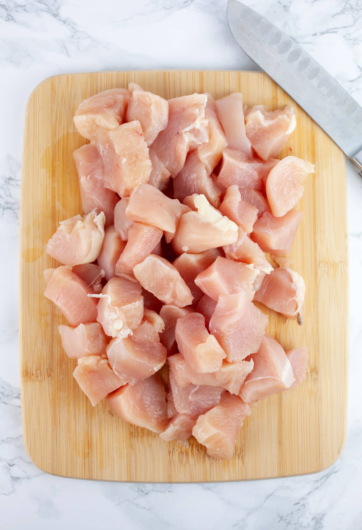 Diced raw chicken breasts on wooden cutting board with knife.
